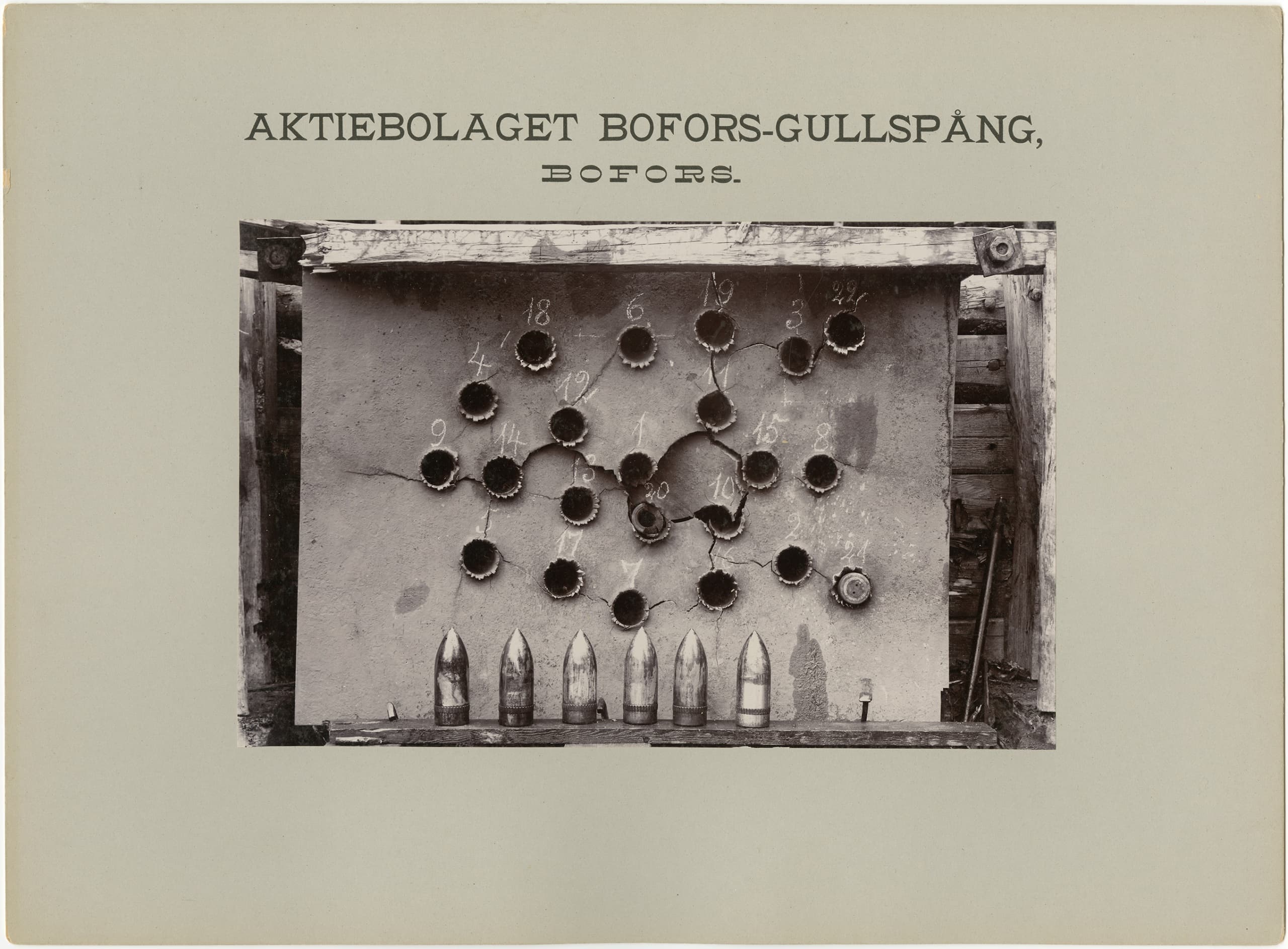 Fotografi monterat på ett kort med texten ”AKTIEBOLAGET BOFORS-GULLSPÅNG, BOFORS.” Visar en metallplåt med flera hål i olika storlekar, numrerade ovanför. Nedanför står flera projektiler uppradade. Bilden har teknisk och dokumenterande karaktär.